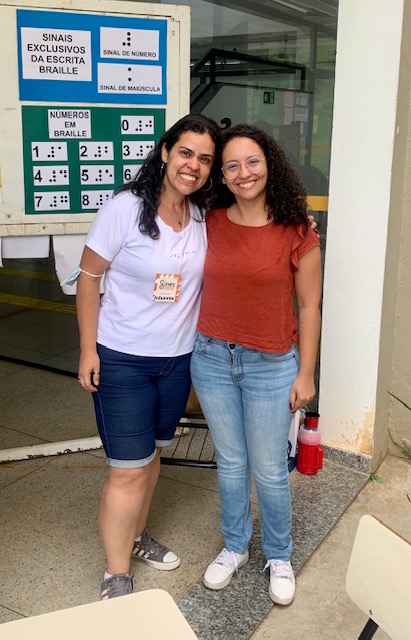 Fotografia de Fernanda e uma participante da interveno em frente a um cartaz com o alfabeto braille.